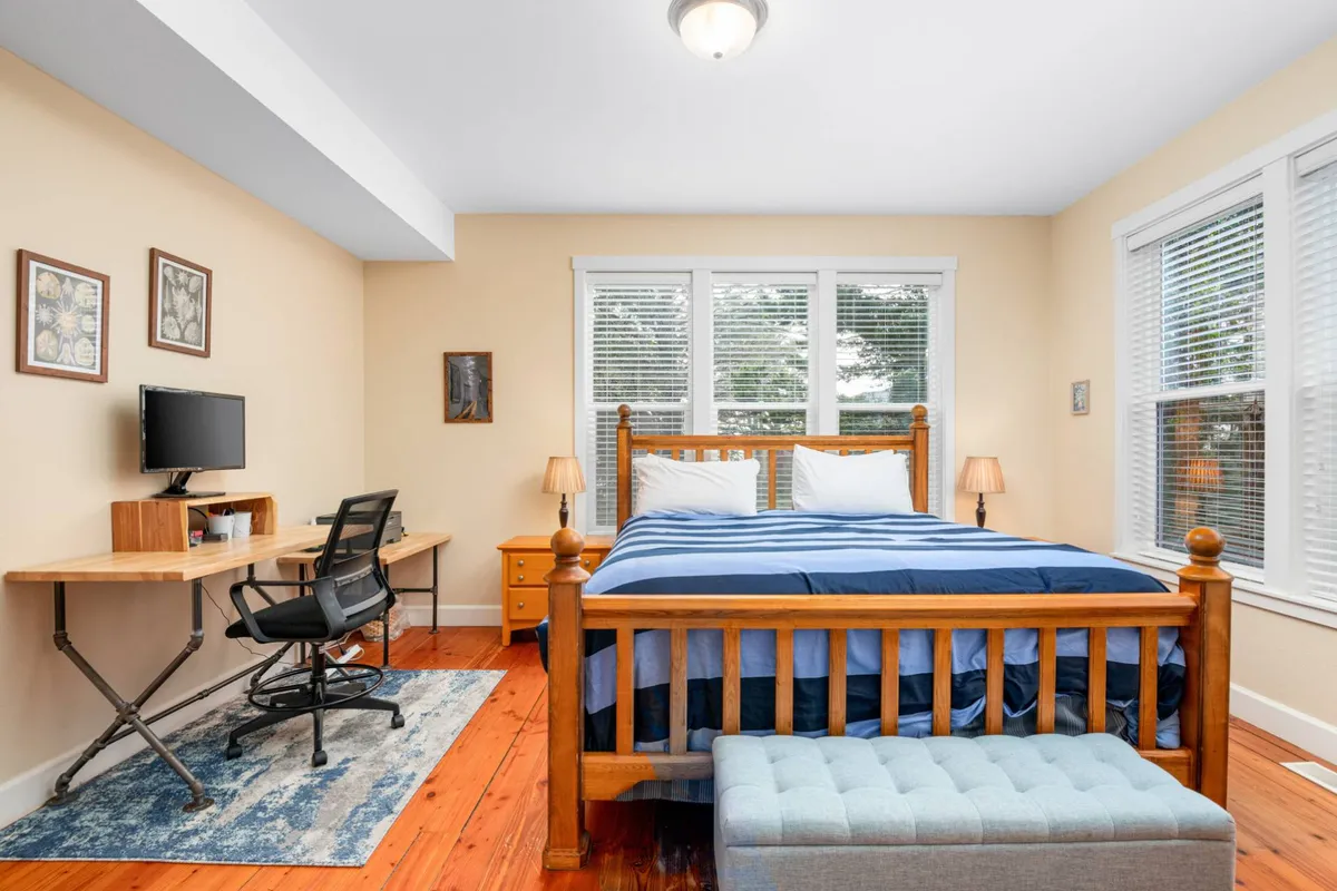 A calm bedroom featuring a bed, a desk with computer, a window with natural light, and artwork, highlighting options for quiet, focused work or relaxation between team activities.