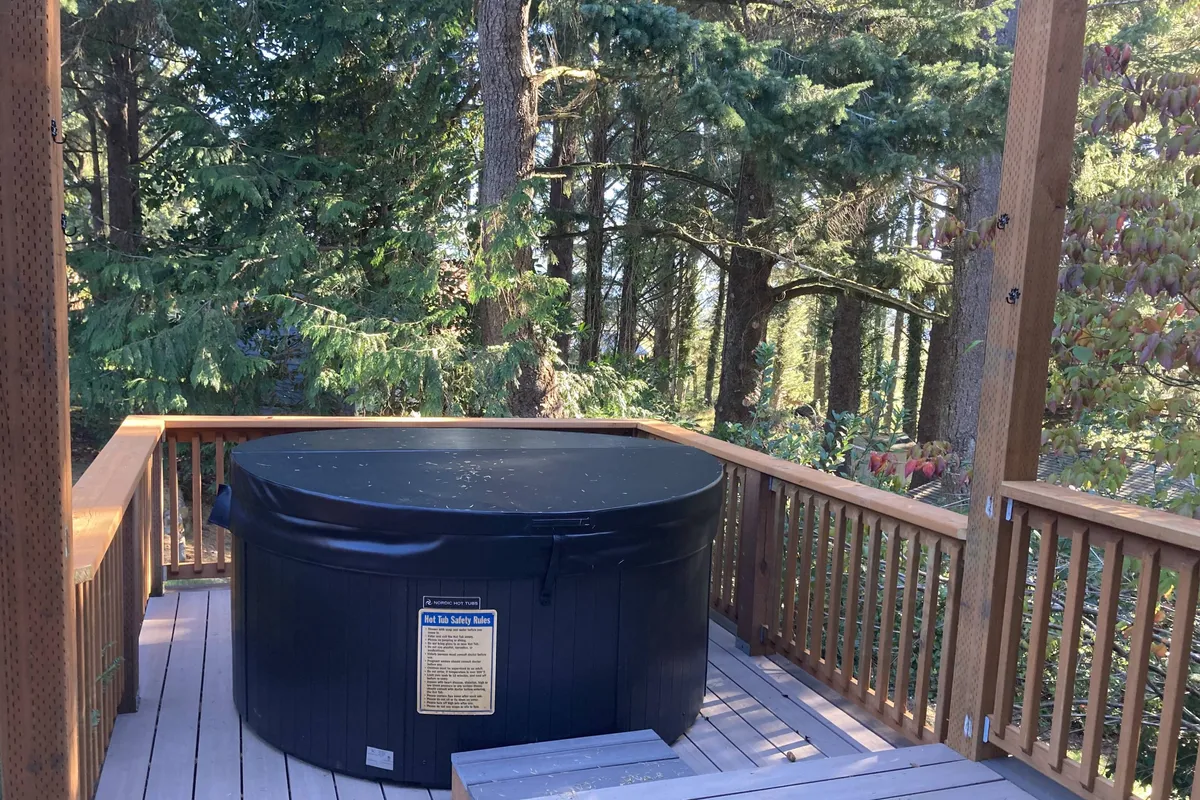 A peaceful scene featuring a bubbling hot tub on a wooden deck surrounded by tall, mature trees. The setting is private and tranquil, inviting guests to unwind while enjoying views of nature. The hot tub is the clear focal point, with the surrounding greenery enhancing the sense of retreat.