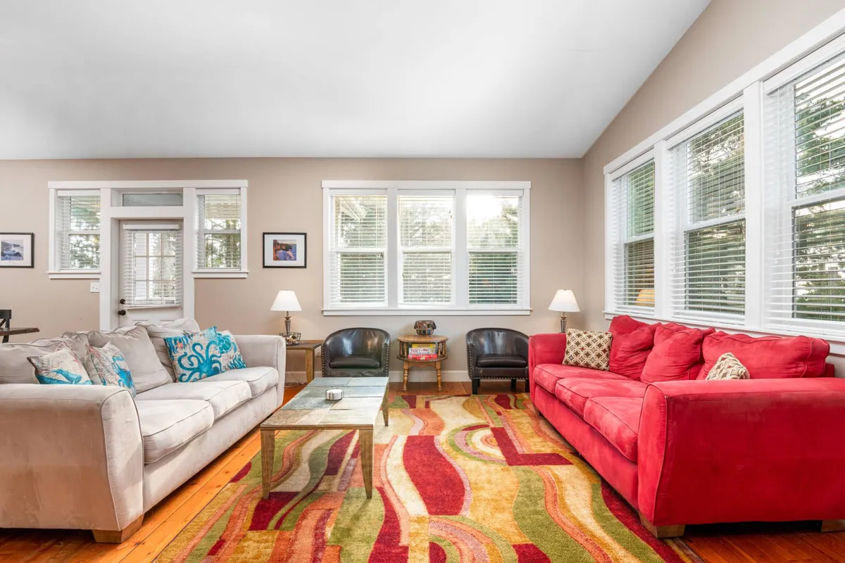 A cheerful great room with a red sofa, colorful rug, large windows letting in natural light, and a coffee table, suggesting a lively environment for group gatherings and team discussions.