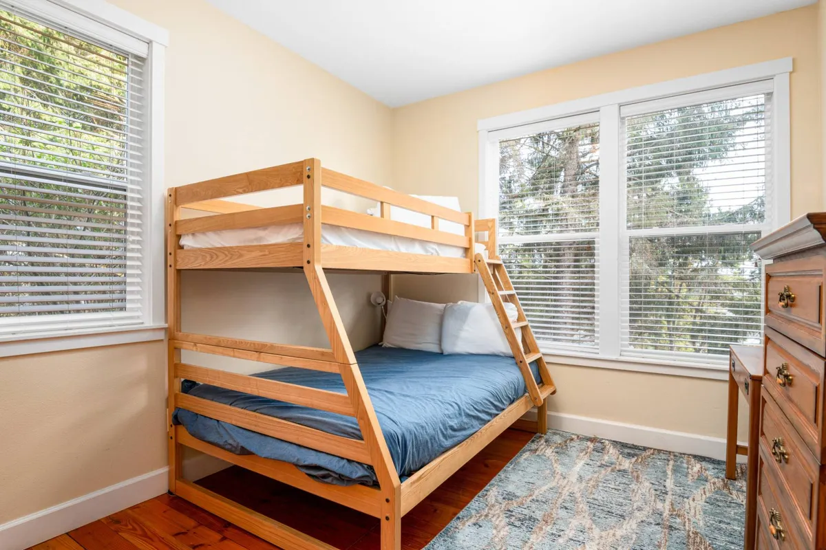 A playful and comfortable bunk room filled with natural light, featuring a sturdy bunk bed, a decorative rug for cozy play, and a wooden dresser. The space feels welcoming for children and families, encouraging bedtime stories and games.