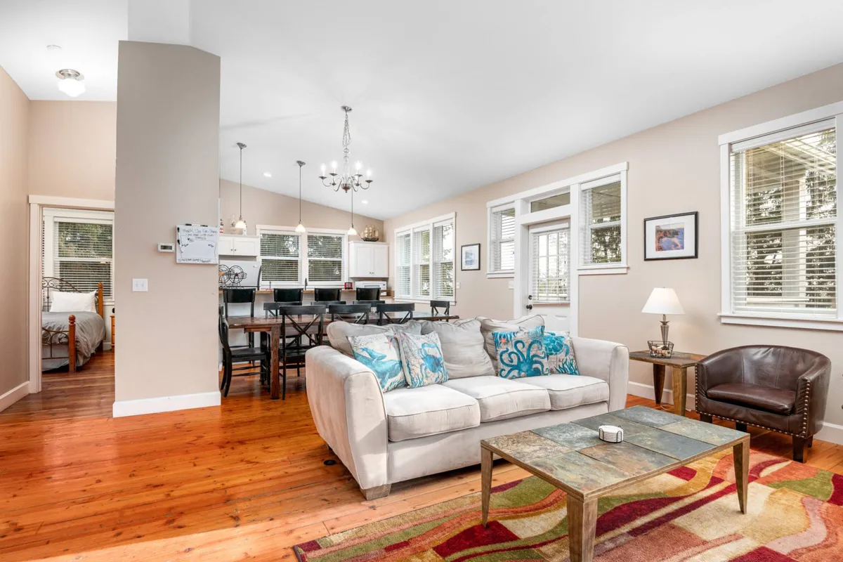 This image captures the heart of the living space, featuring a sofa with decorative cushions, a prominent dining table, and a view of the kitchen counter. The open-concept layout enables easy flow between lounging, dining, and cooking areas, reflecting the communal spirit described in the section.