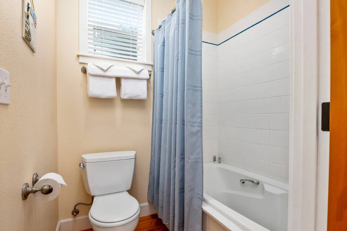 A clean, refreshing full bathroom featuring a bathtub, shower curtain, toilet, and fluffy towels. The serene atmosphere suggests comfort and convenience for guests after active play or beach days.