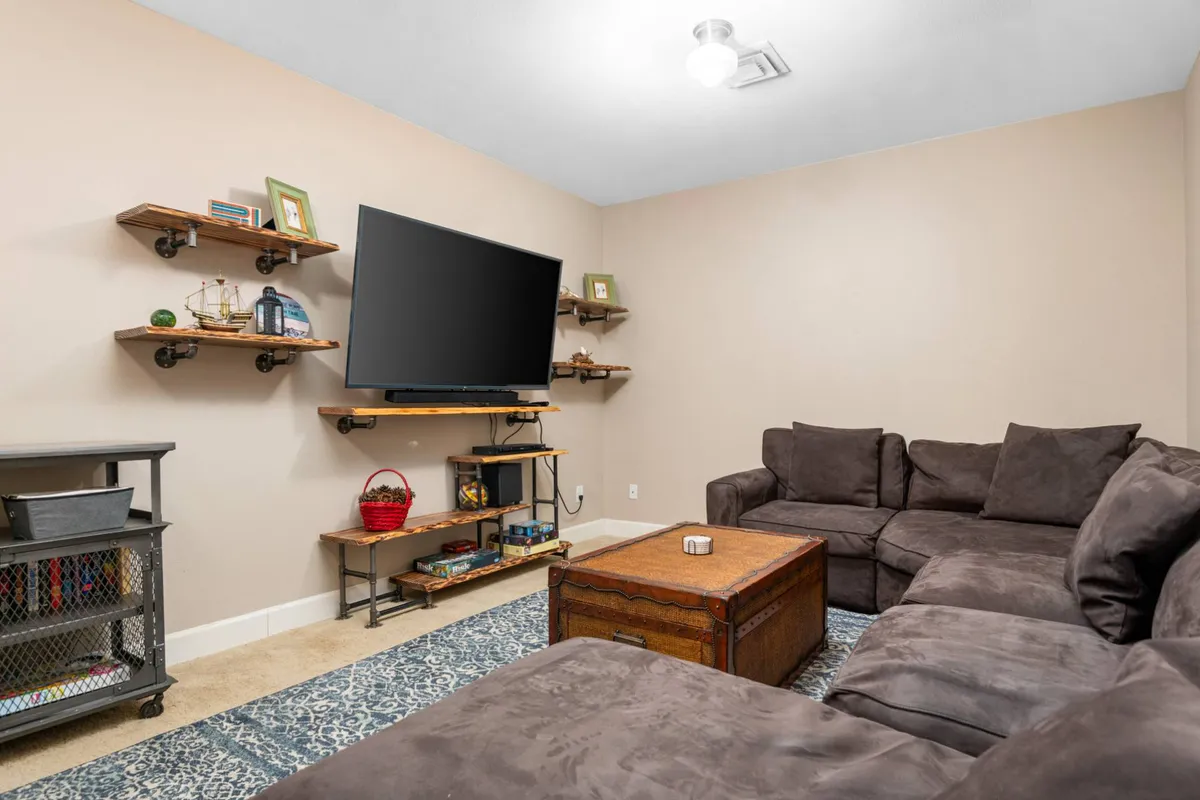 A cozy family room centered around a large television, with a comfortable sofa, wooden coffee table, and decorative shelves holding books and games. The space is inviting and relaxed, encouraging group activities, movie nights, and all-ages hangouts.