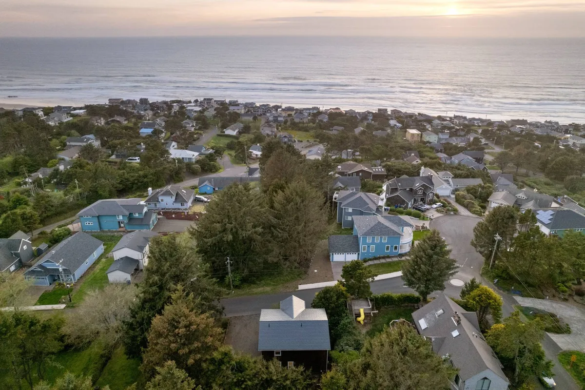 A wide view capturing the ocean, a line of trees, and a tranquil cluster of houses. This perspective highlights the neighborhood’s scenic beauty and hints at the nearby attractions and experiences that guests can explore.