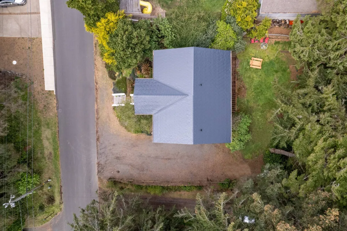 A peaceful backyard scene featuring a spacious green lawn, surrounding trees, and a welcoming space perfect for gatherings or play. The area is ideal for spotting deer, letting kids play, or unwinding after a day at the beach.