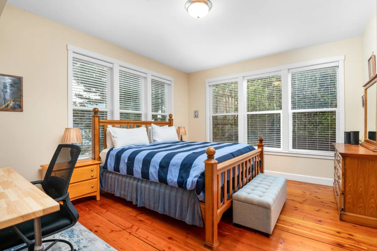 A serene bedroom featuring a spacious bed with plush linens, large windows that invite natural light and showcase sunrise views, a sleek desk ideal for working or enjoying morning coffee, and a dresser for extra storage. The calming palette and uncluttered layout make it perfect for rest or productivity.